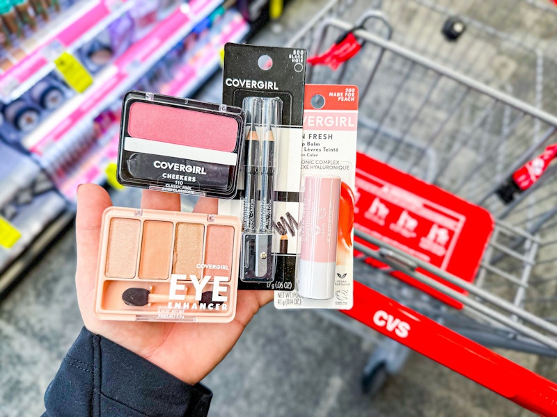 person holding covergirl eyeshadow, blush, eyeliner, and lip balm over a cvs cart