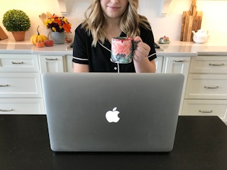 A woman sitting in front of her laptop in her pajamas holding a cup of coffee