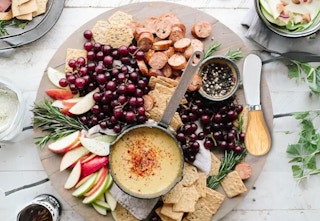 a birds-eye view of a charcuterie board with cheese spreader, fruit, meat, and crackers
