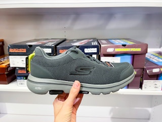 someone holding a dark pair of men's skechers shoes