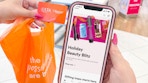 a woman holding a ulta bag and ulta credit card and a cellphone with app with holiday blitz on screen