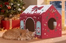 a cat sleeping next to a cardboard Christmas-themed cat house in a room