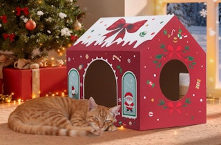 a cat sleeping next to a cardboard Christmas-themed cat house in a room