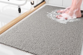 Lifestyle image of the Sixhome Non-Slip Shower Mat in the color gray (close up shot of someone standing on it with soap suds around feet)