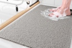 Lifestyle image of the Sixhome Non-Slip Shower Mat in the color gray (close up shot of someone standing on it with soap suds around feet)