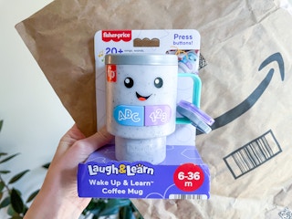 a hand holding a toy coffee mug in front of an Amazon mailer