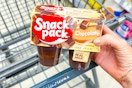 person holding a package of snack pack pudding over a cart