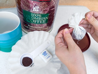 Someone tying a coffee filter filled with coffee grounds with some dental floss