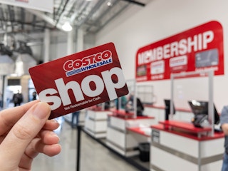 A person's hand holding up a Costco Shop card near the the membership counter.