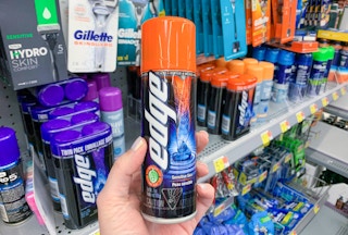 A hand holding a can of Edge shaving cream in front of a shelf of other shaving creams at Walmart.