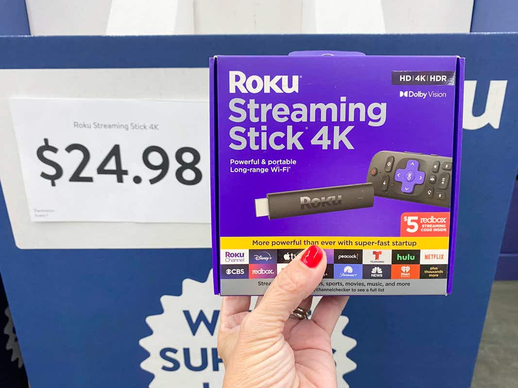 a woman's hand holding up a Roku streaming stick 4K next to a $24.98 sale price at Walmart