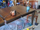 A dinning table with stain and a sander on top of it.