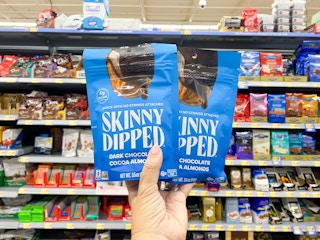 hand holding two blue bags of SkinnyDipped almonds in the snack aisle at Walmart