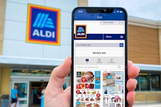 Someone holding their phone displaying the ALDI app in front of an ALDI store