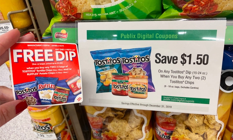 Hand holding a paper coupon for Tostitos and Ruffles next to a sign for Publix digital coupons