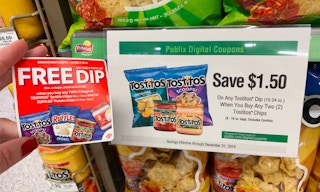 Hand holding a paper coupon for Tostitos and Ruffles next to a sign for Publix digital coupons