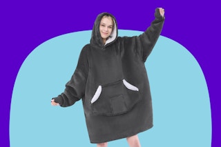 A woman in a grey fleece blanket sherpa lined hoodie with a front pocket holds out her arms.