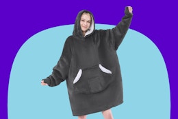 A woman in a grey fleece blanket sherpa lined hoodie with a front pocket holds out her arms.