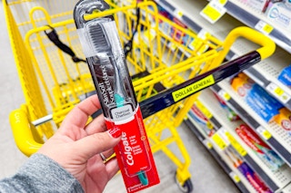hand holding colgate charcoal toothbrush next to dollar general shopping cart
