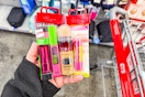 person holding maybelline lipstick, mascara, foundation, and baby lips by a cart