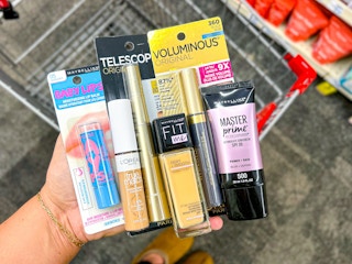 hand holding l'oreal and maybelline cosmetics over a shopping cart