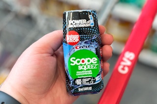 hand holding bottle of mouthwash concentrate above cvs shopping cart