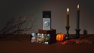 Official promotional banner from Ring showing a doorbell on top of a box with a phone displaying camera feed and halloween decor.