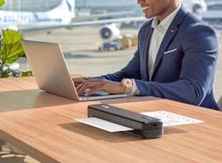 a person sitting at a table on a laptop next to a mini printer