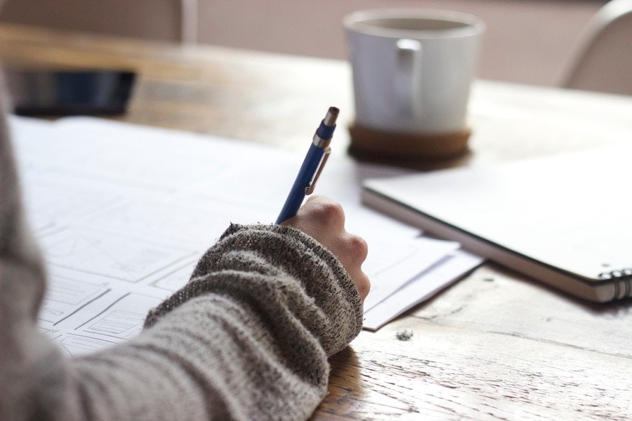 woman writing on paper with pen at table