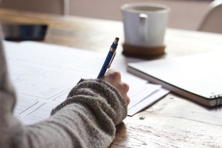 woman writing on paper with pen at table
