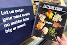 person holding hy-vee grocery catering guide next to banner