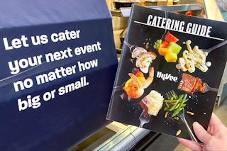 person holding hy-vee grocery catering guide next to banner