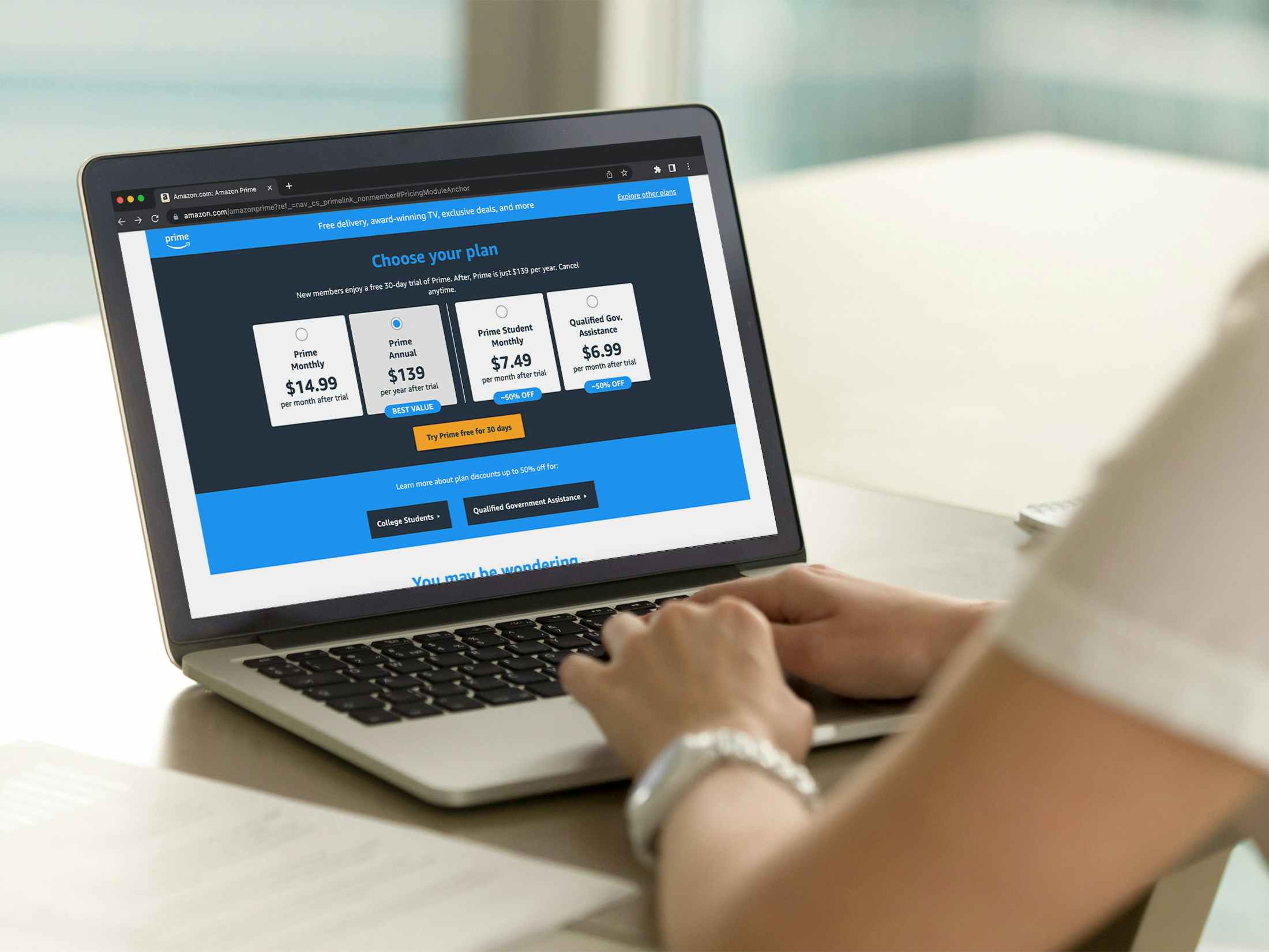 A person using a laptop with the Amazon Prime subscription plan options displayed on the screen.