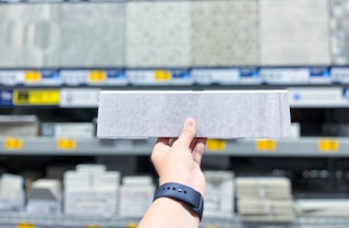 Tile selection held up in front of other sizes and colors of tile isle in stores at Lowe's