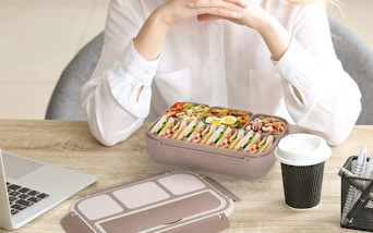 a person eating food from a bento box at a desk