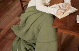 a person sitting at a wooden table with a green electric blanket 