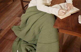 a person sitting at a wooden table with a green electric blanket 