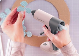 a person using a pink hot glue gun on a paper flower