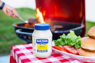 best foods like hellmann's mayo on table in front of burgers on the grill 