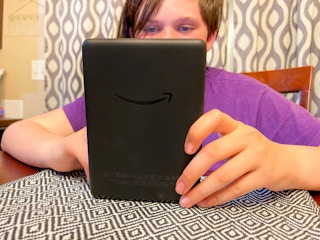 a teen reading on a kindle at the table