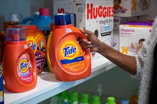 A person pulling a bottle of Tide laundry detergent off a stockpile shelf in a storage room.