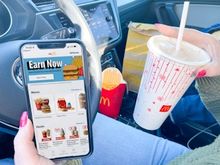 Hand holding a phone with the McDonalds app on it and fries and a drink in the background