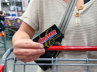 a person holding a costco cart while psuhing cart