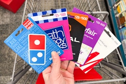 person holding dominos, bath and body works, regal, wayfair, and h&m gift cards over a cart