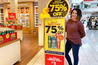 A woman standing next to a sign outside of Bath & Body Works advertising their 75% off Semi-Annual clearance sale.