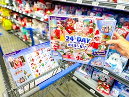 hand holding an elf on the shelf ultimate kit with another one in a walmart cart