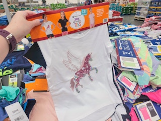 a hand holding a set of 3 kids tees. the one in front is white with a sparkly unicorn