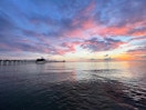 sunset on the ocean from the beach with a long pier on in the background