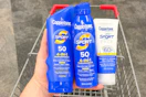 hand holding three coppertone sunscreens over a shopping cart