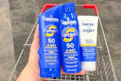 hand holding three coppertone sunscreens over a shopping cart